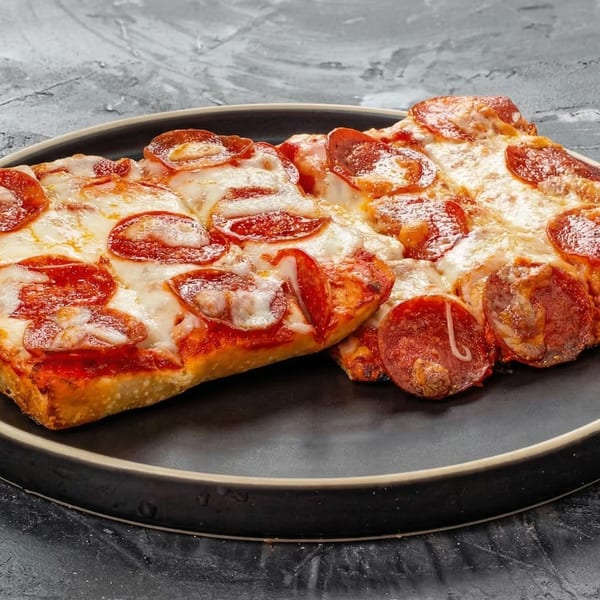 Two rectangular slices of New York-style pepperoni pizza with melted cheese on a dark plate.