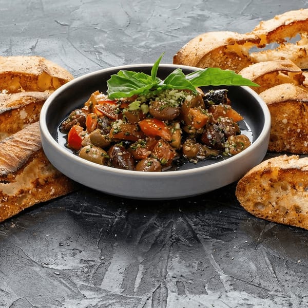A bowl of marinated olives and tomatoes, garnished with basil, surrounded by crusty bread.